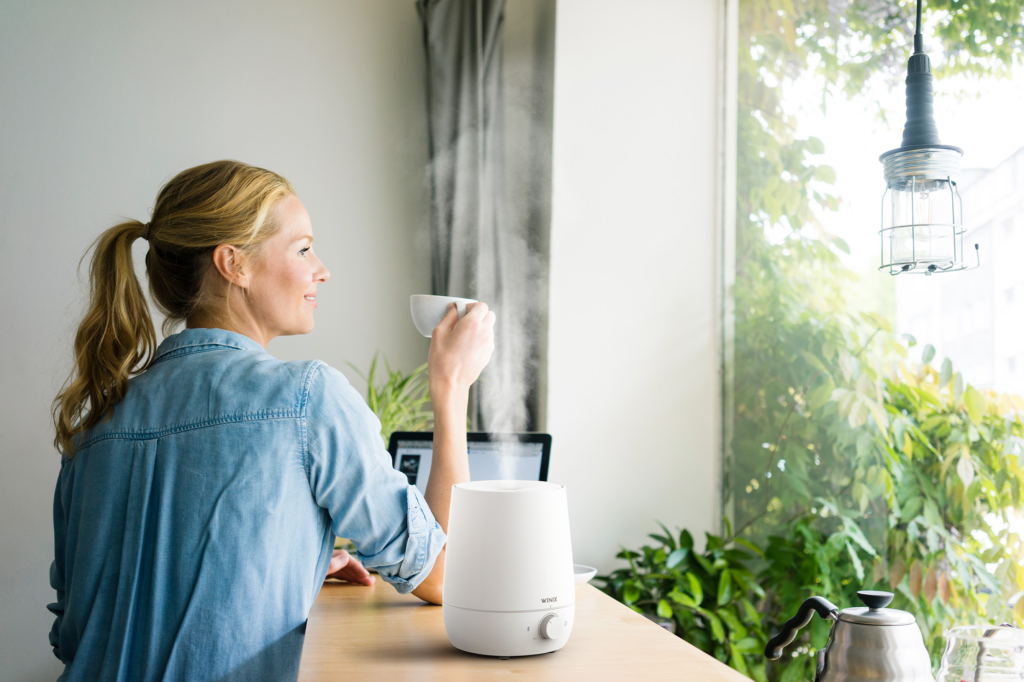 Woman sitting at her home office desk surrounded by houseplants with steam coming out of L60 humidifier