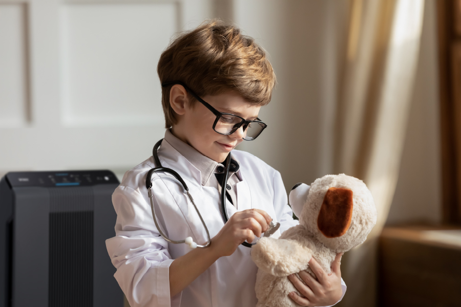 Boy in doctors outfit using a stethascope on stuffed animal with 5500-2 air purifier in background