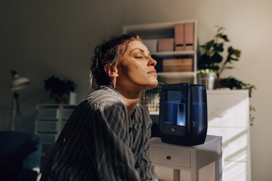 Woman sitting in bedroom with eyes closed while L200 Humidifier soothes her