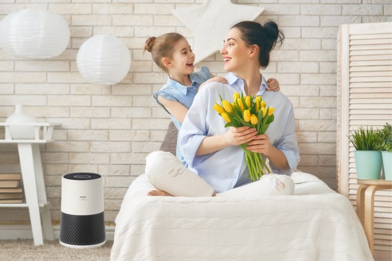 Mother and daughter sitting on bed with flowers while A231 Air Purifier cleans from floor next to bed.