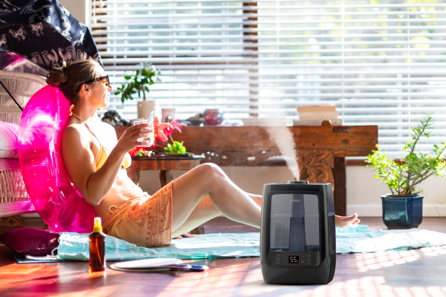 Woman sitting on floor in room sun tannning through winow with L200 Humidifier next to her
